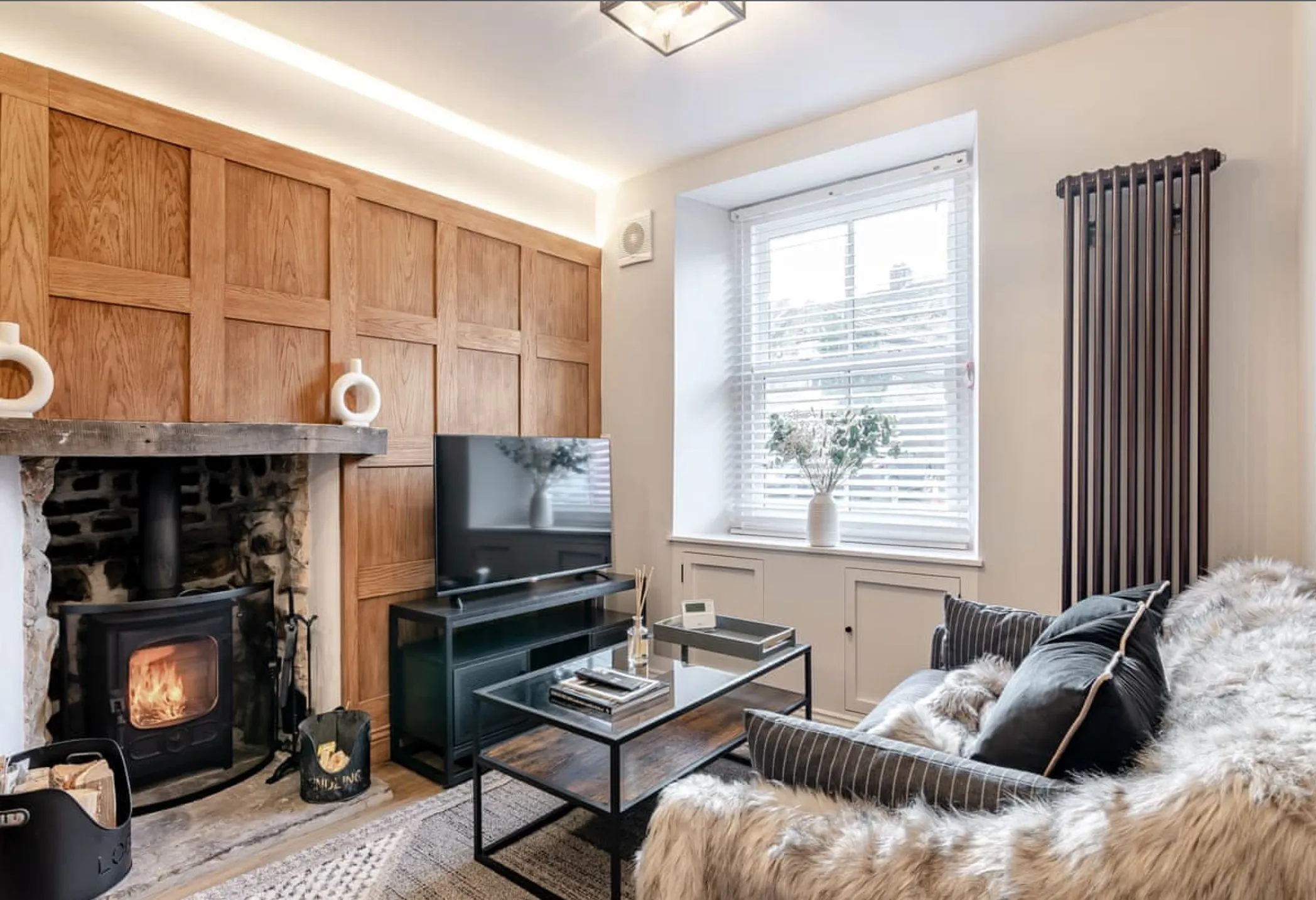 Oak-panelled sitting room with the wood burner lit, a fur-throw sofa and sash window
