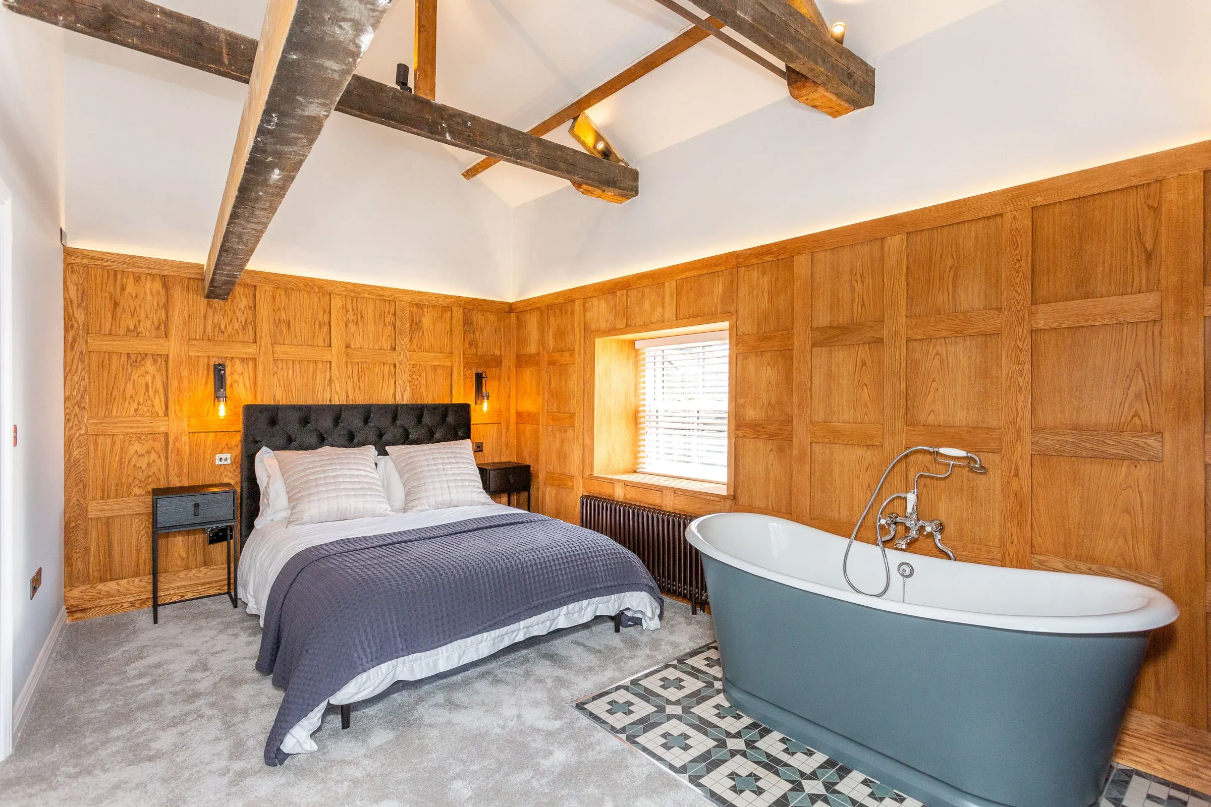Vaulted bedroom with oak panelling, exposed beams and a freestanding roll-top bath