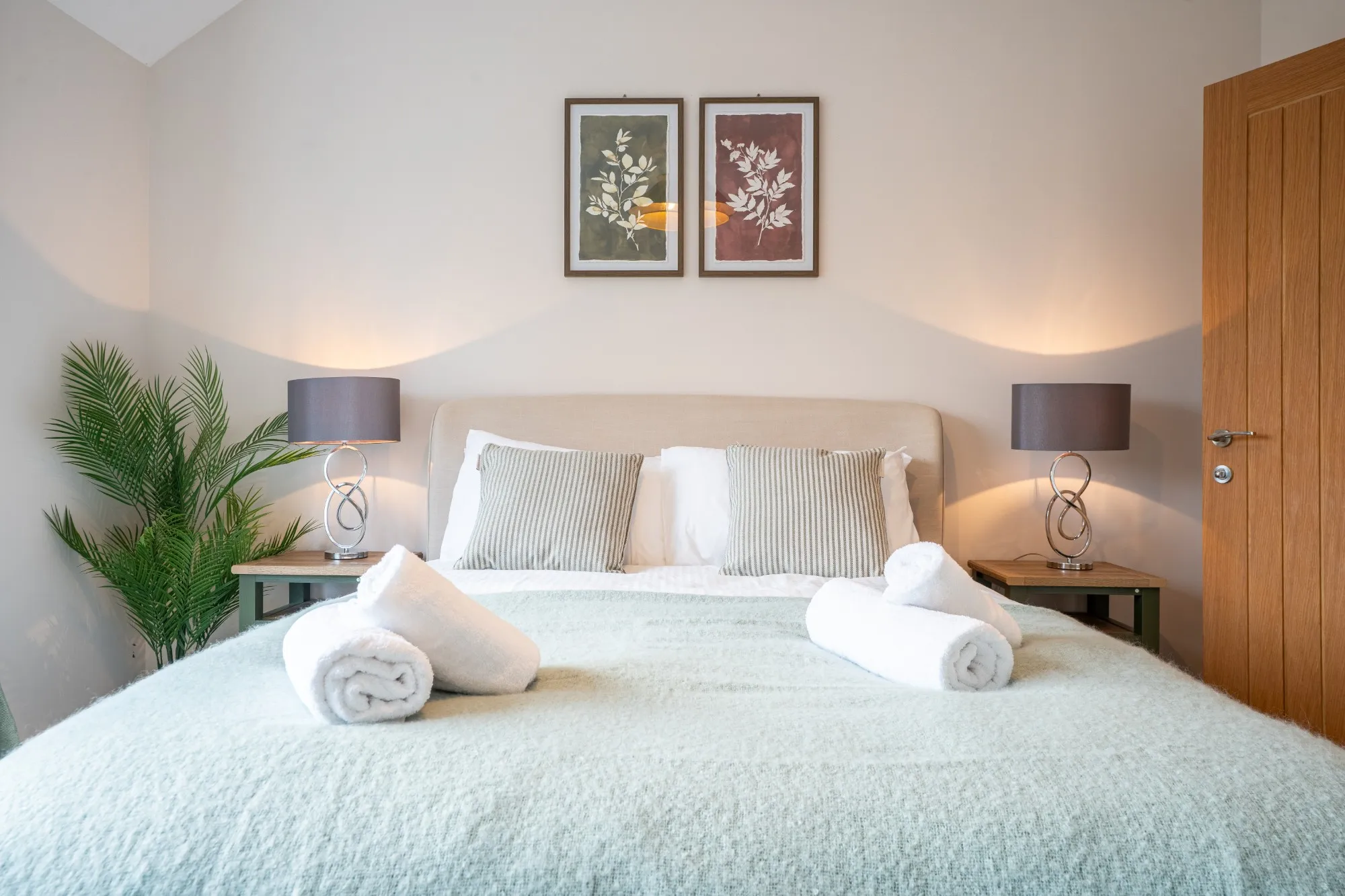 The bed made up with rolled towels, striped cushions and a pair of botanical prints above