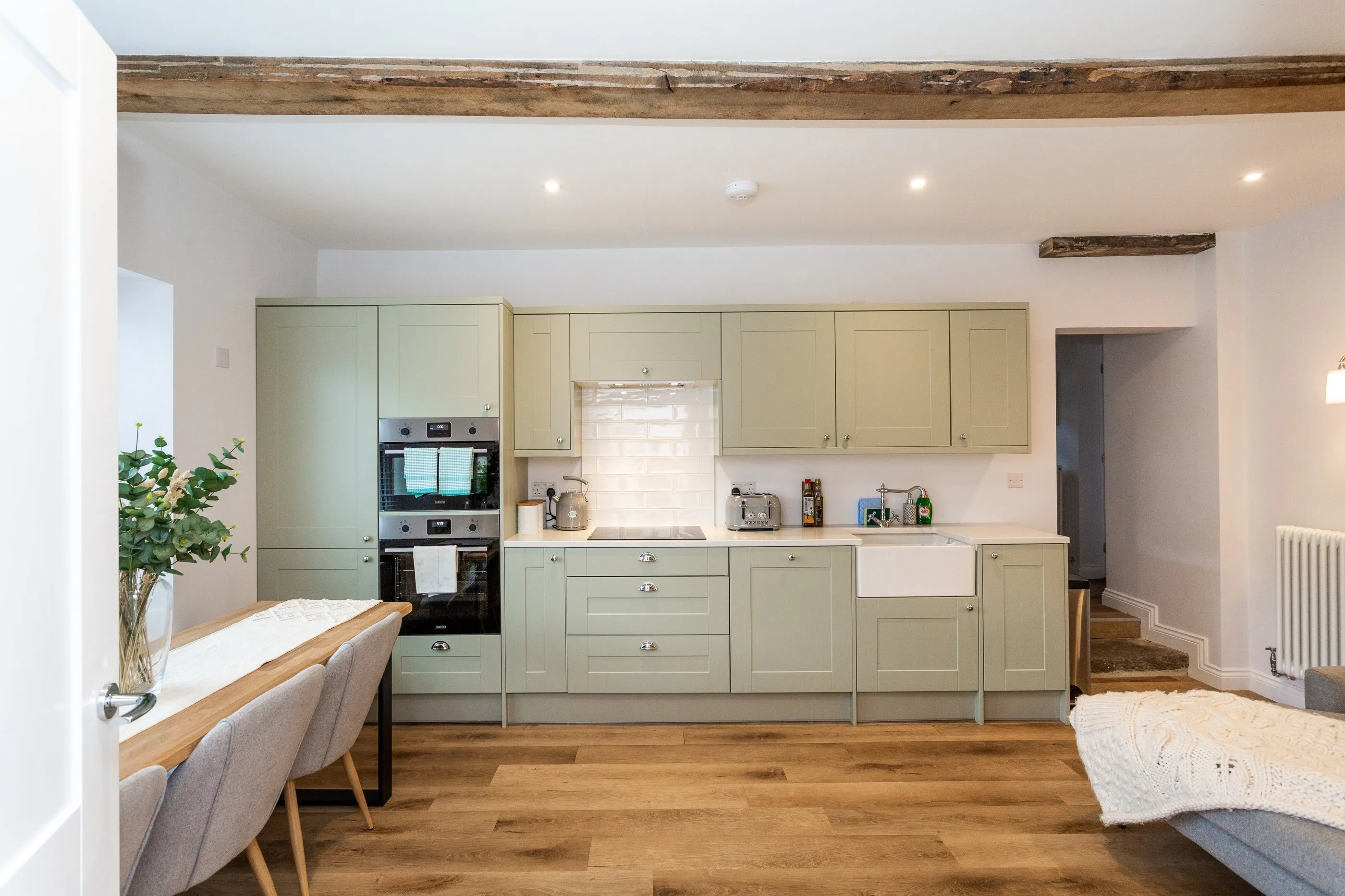 Sage-green shaker kitchen with Belfast sink, double ovens and oak beam