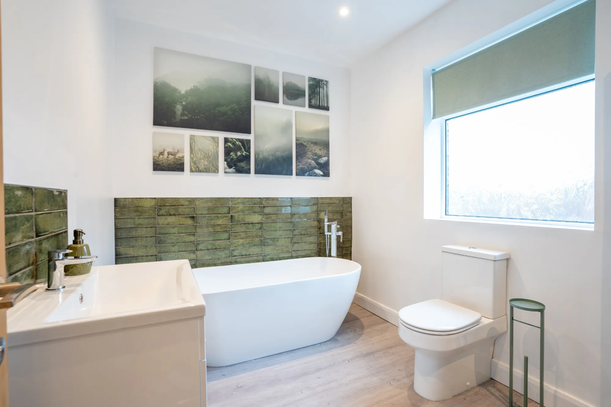 Bathroom with a freestanding bath, green glazed tiles and a wall of woodland prints