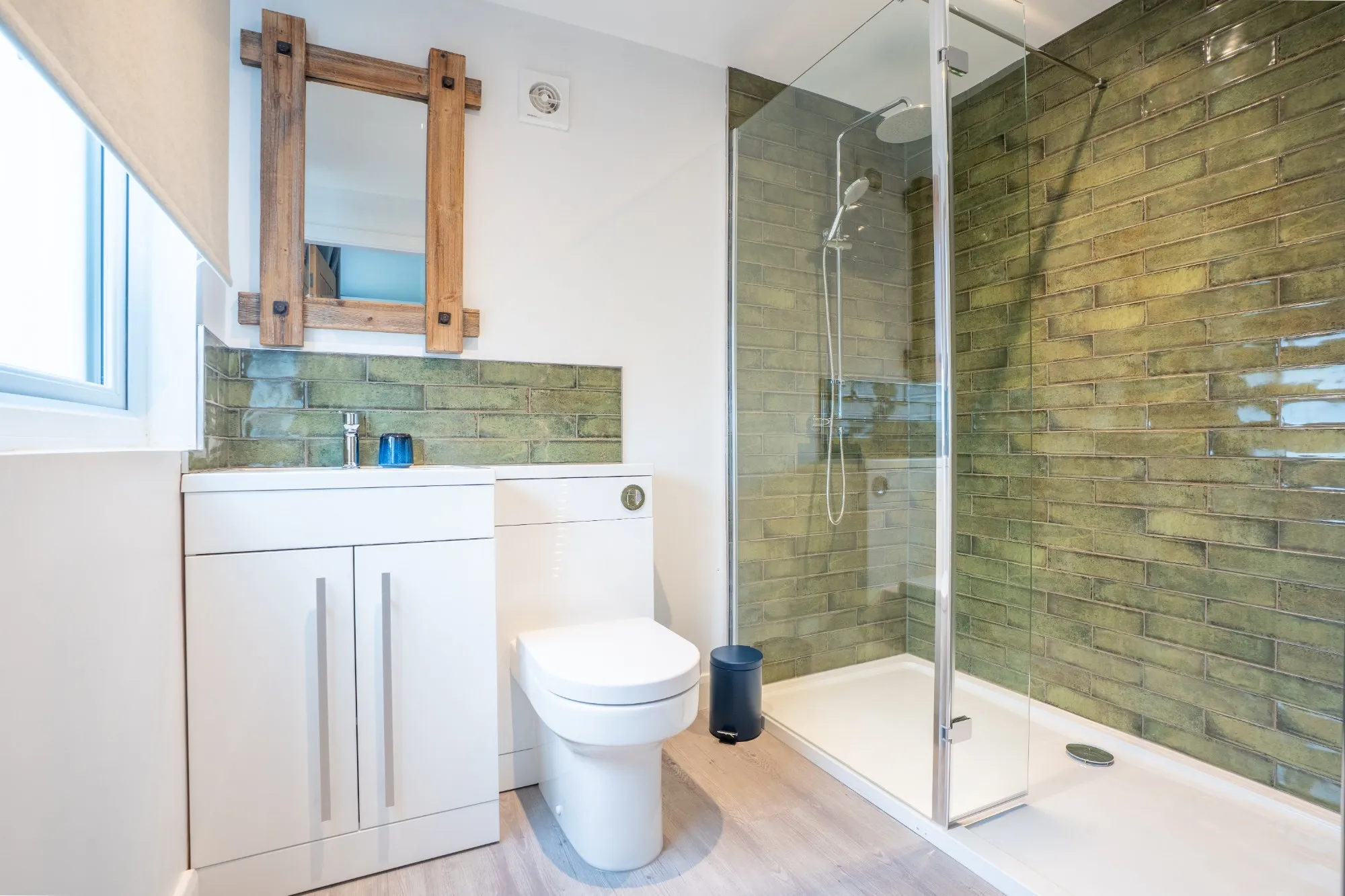 Shower room with a walk-in shower in olive glazed tiles, a white vanity unit and a rustic timber mirror