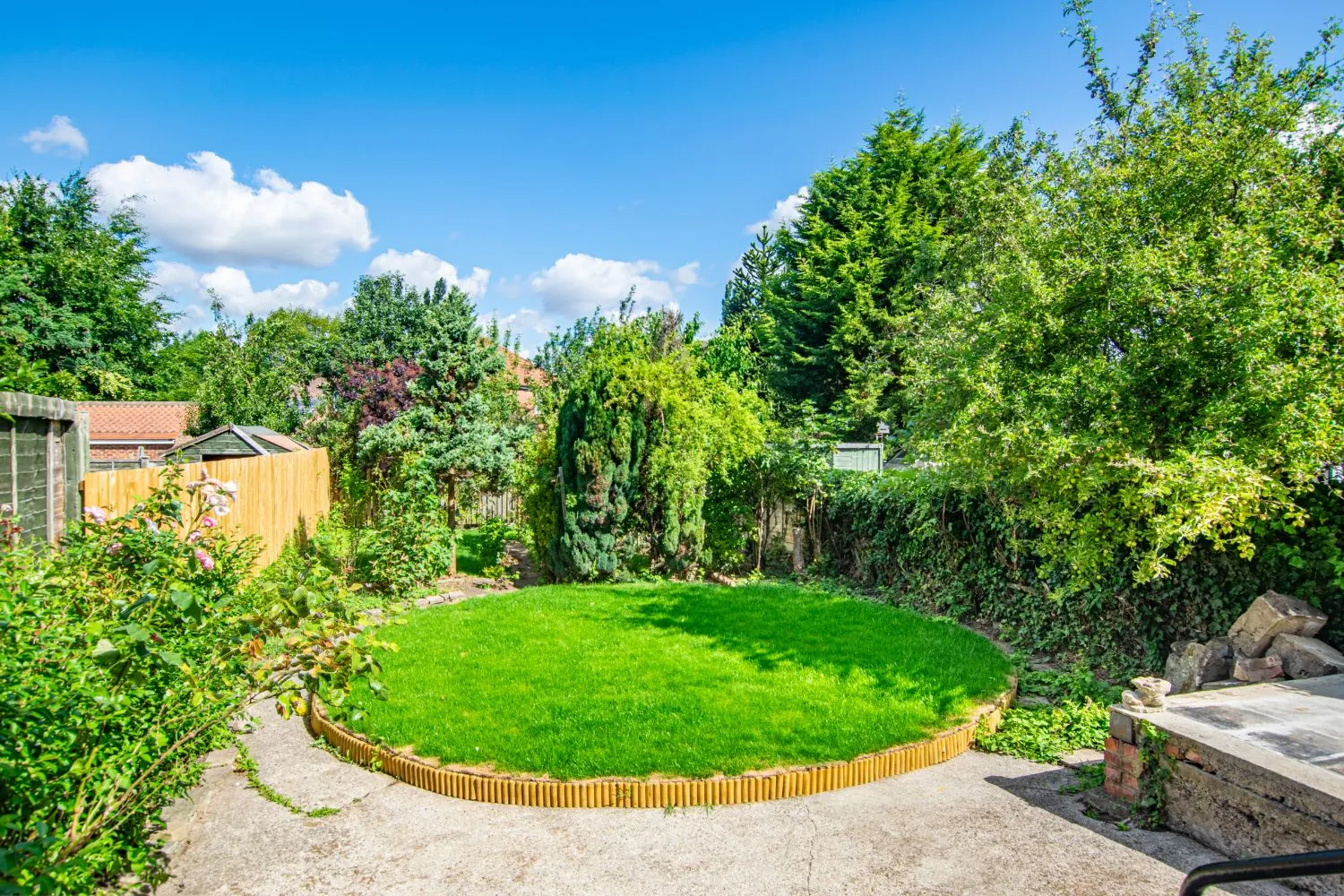 The back garden: a round lawn edged in timber, roses, mature trees and hedges