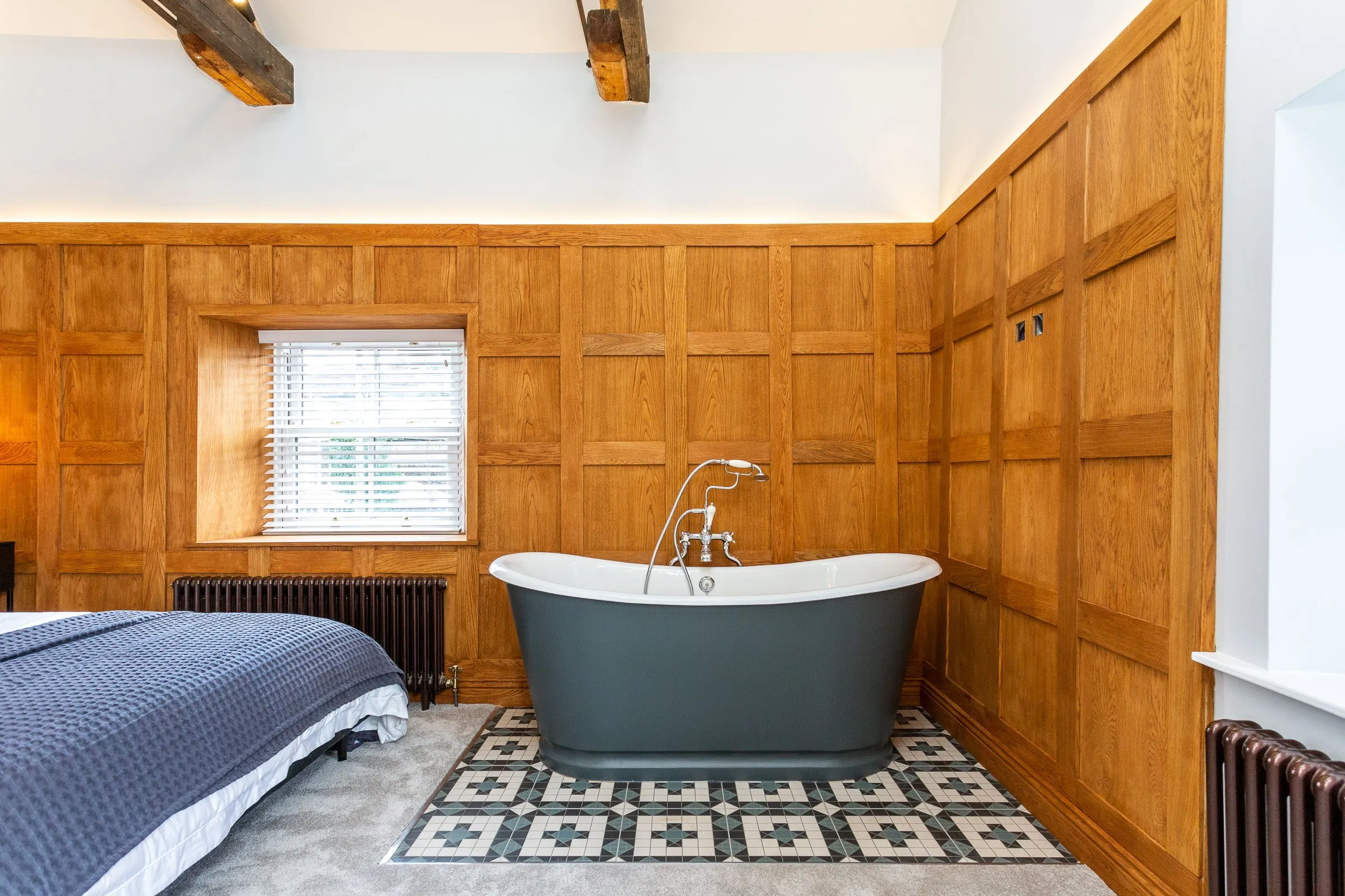 Freestanding roll-top bath on patterned tiles in the bedroom