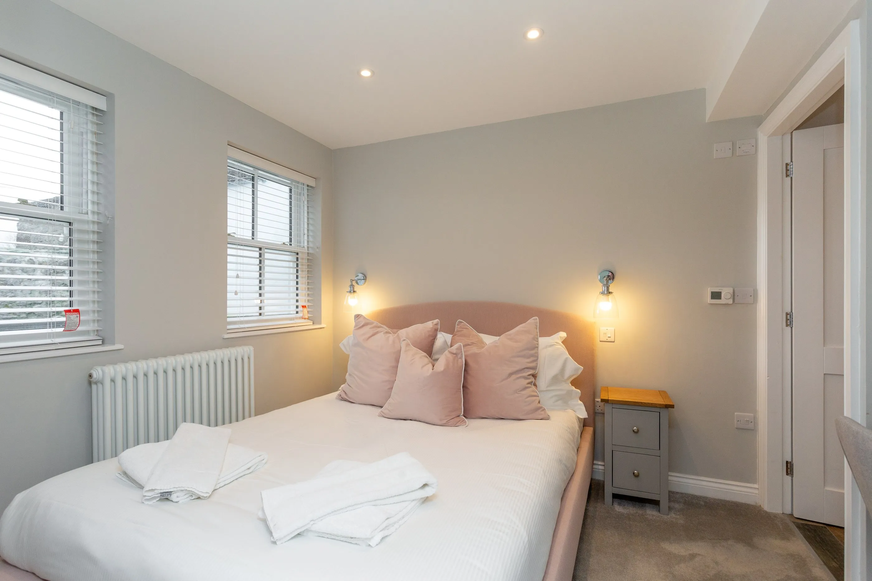 Ground-floor bedroom with blush headboard, wall lights and en suite