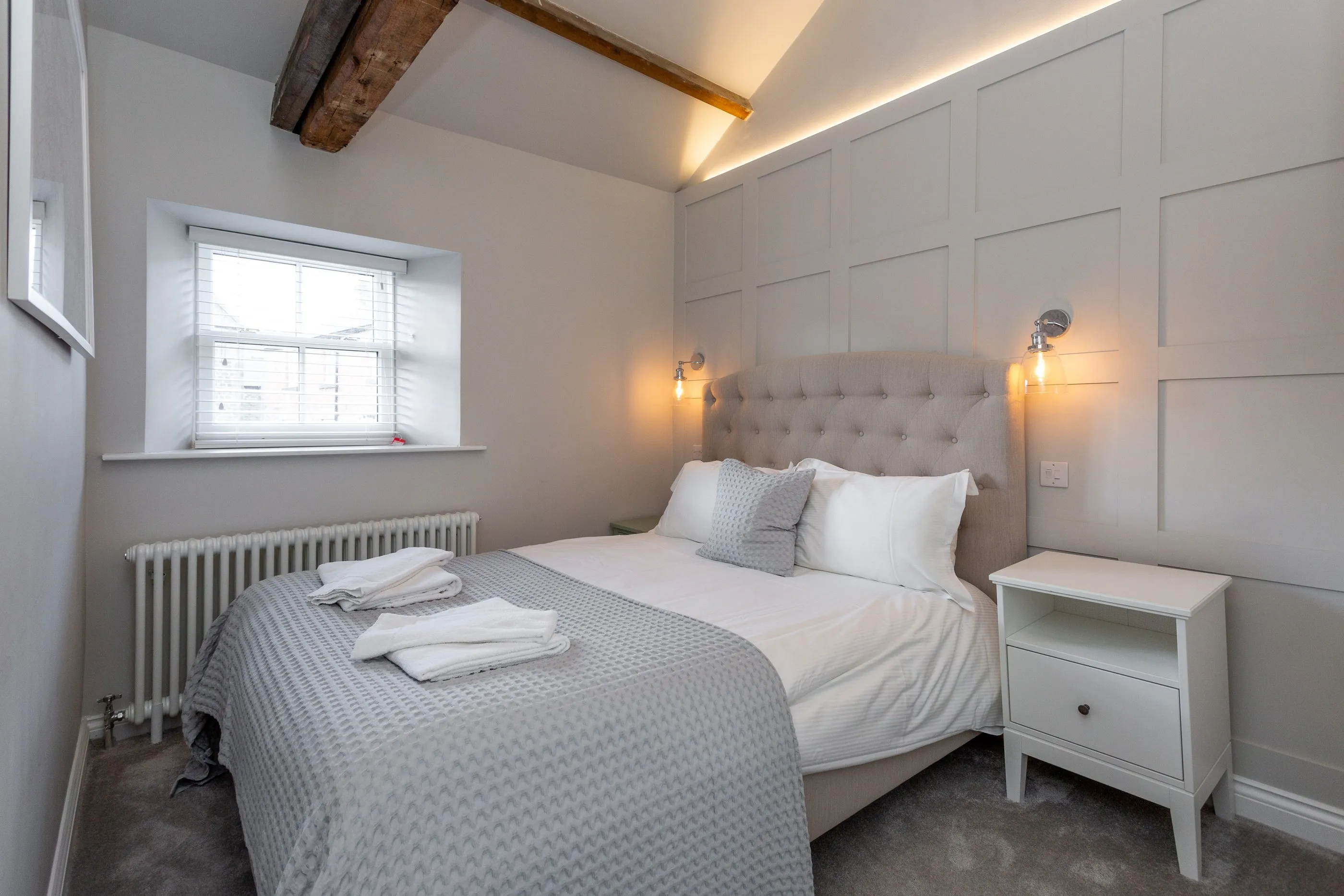Bedroom with tufted headboard, panelled wall and exposed beam