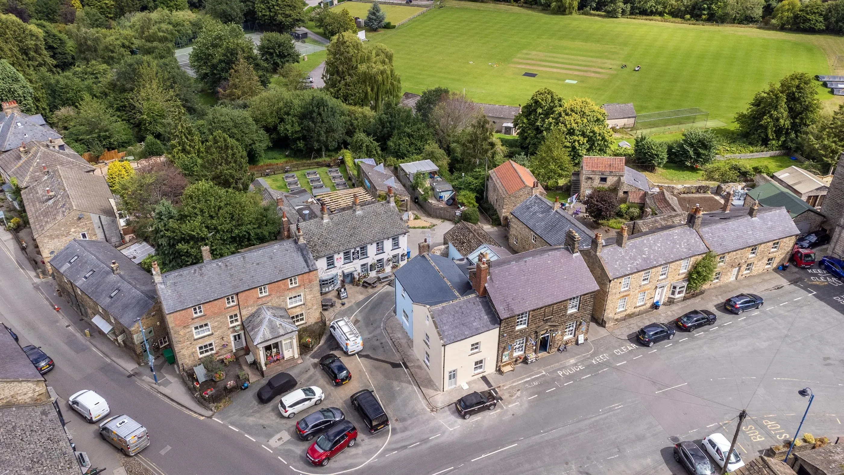 The cottage and neighbouring Bruce Arms from above, with the cricket ground behind