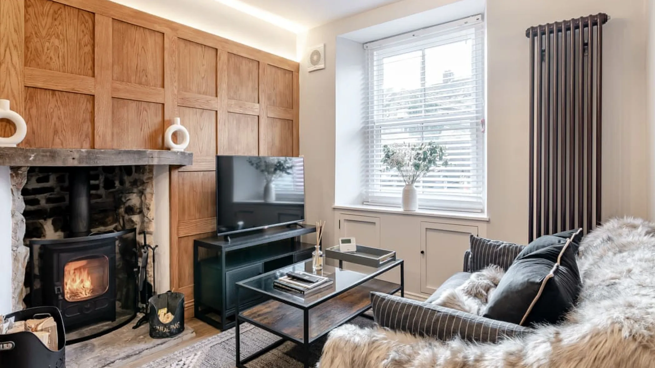 Oak-panelled sitting room with the wood burner lit, a fur-throw sofa and sash window